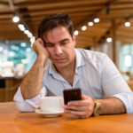 Man at a coffee shop engrossed in mobile phone, reminiscent of modern customer service trends.