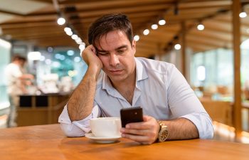 Man at a coffee shop engrossed in mobile phone, reminiscent of modern customer service trends.